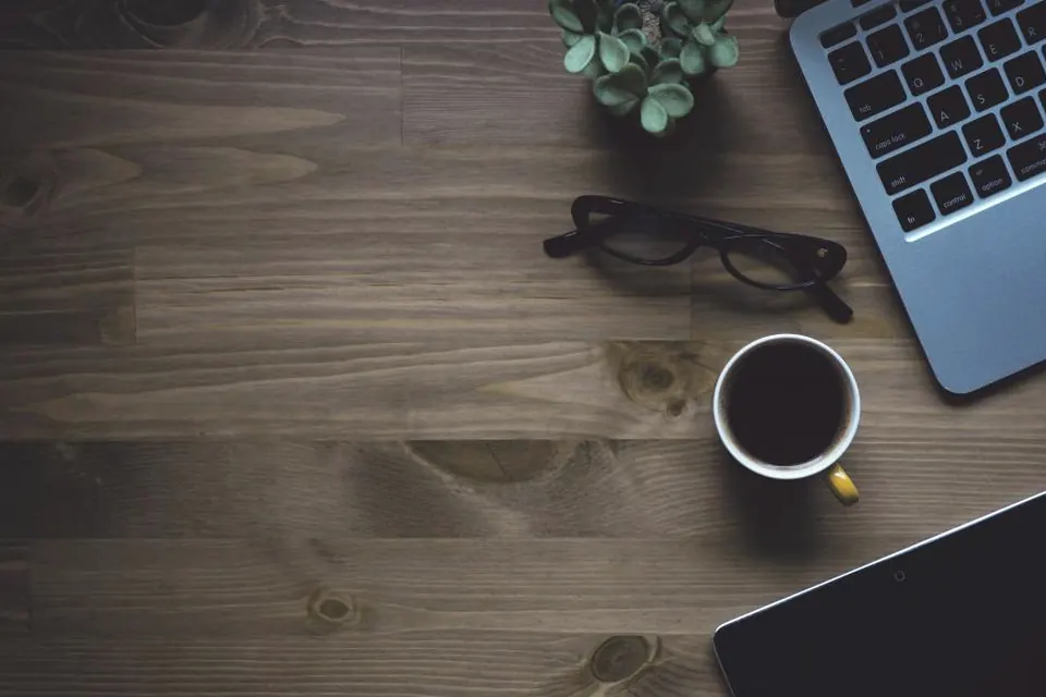 A desk with a laptop, glasses and a cup of coffee.